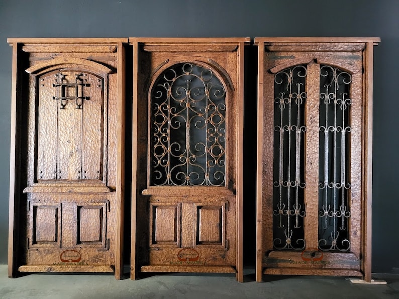 May include: Three wooden doors with intricate ironwork details. The doors are all different styles, with one featuring a simple square design, another with a more ornate scroll design, and the third with a double door design with vertical bars. The doors are all made of dark wood and have a rustic look.