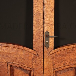 Puede incluir: Primer plano de una puerta doble de madera con un dise&ntilde;o tallado. La puerta tiene una manija de puerta de metal y una cerradura. La puerta est&aacute; hecha de madera marr&oacute;n claro con un acabado r&uacute;stico.