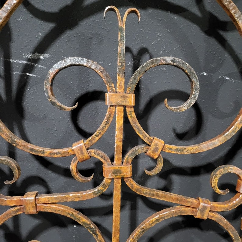 May include: A close-up of a decorative metal gate with a rust-coloured finish. The gate is made of wrought iron and features an intricate design of scrolls and curves.