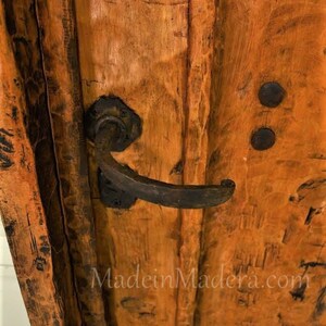 Puede incluir: Primer plano de una puerta de madera con un acabado marr&oacute;n oscuro envejecido. La puerta tiene un tirador de metal negro y dos bisagras de metal negro. El texto "MadeinMadera.com" es visible en la puerta.