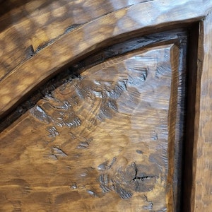 May include: Close-up of a dark brown wooden door with a rounded top and a raised panel. The wood has a rustic, distressed look with knots and grain patterns. The door is labelled "MADE IN MADERA" in a white font.