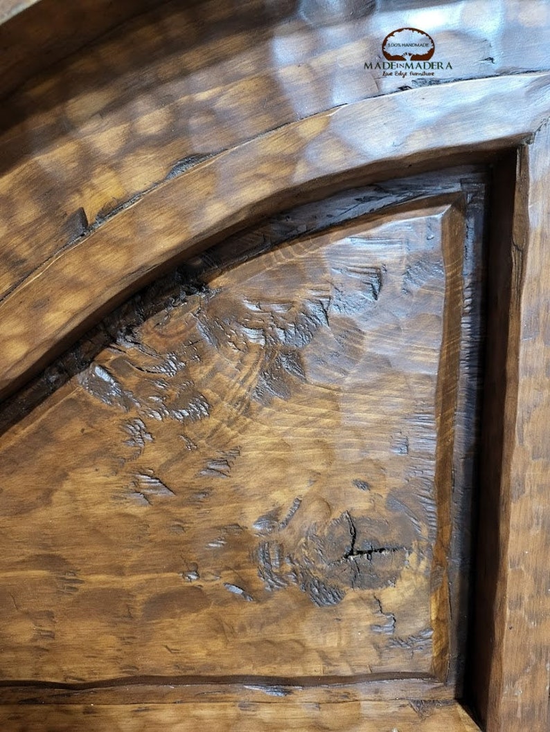 May include: Close-up of a dark brown wooden door with a rounded top and a raised panel. The wood has a rustic, distressed look with knots and grain patterns. The door is labelled "MADE IN MADERA" in a white font.