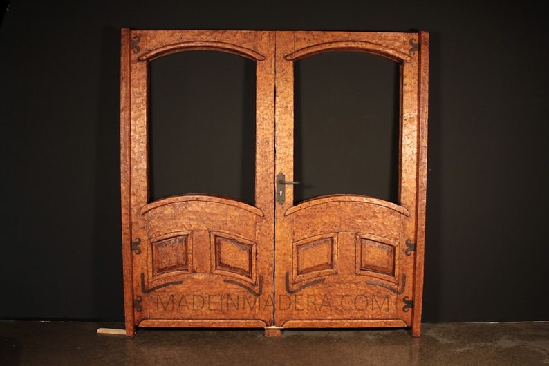 Puede incluir: Un par de puertas dobles de madera con paneles de vidrio arqueados y tallas intrincadas. Las puertas est&aacute;n te&ntilde;idas de un rico color marr&oacute;n y cuentan con una manija y bisagras de metal. Las puertas est&aacute;n etiquetadas con "MADE IN MADERA.COM".