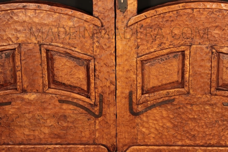 Puede incluir: Primer plano de un par de puertas de madera con intrincados tallados y detalles met&aacute;licos. Las puertas son de un color marr&oacute;n intenso y tienen un aspecto r&uacute;stico y antiguo. El texto "MADE IN" est&aacute; tallado en la parte superior de las puertas.