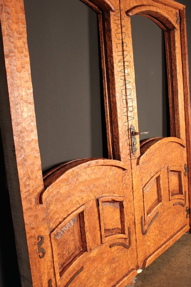 Puede incluir: Un par de puertas dobles de madera con intrincados tallados y paneles de vidrio arqueados. Las puertas est&aacute;n hechas de una madera rica y oscura y tienen un aspecto r&uacute;stico y antiguo.