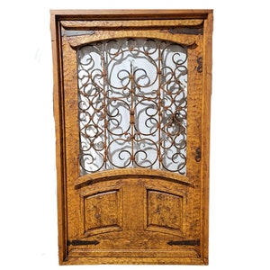 May include: A wooden door with a wrought iron decorative insert. The door is a medium brown colour and has a distressed finish. The door has two panels at the bottom.