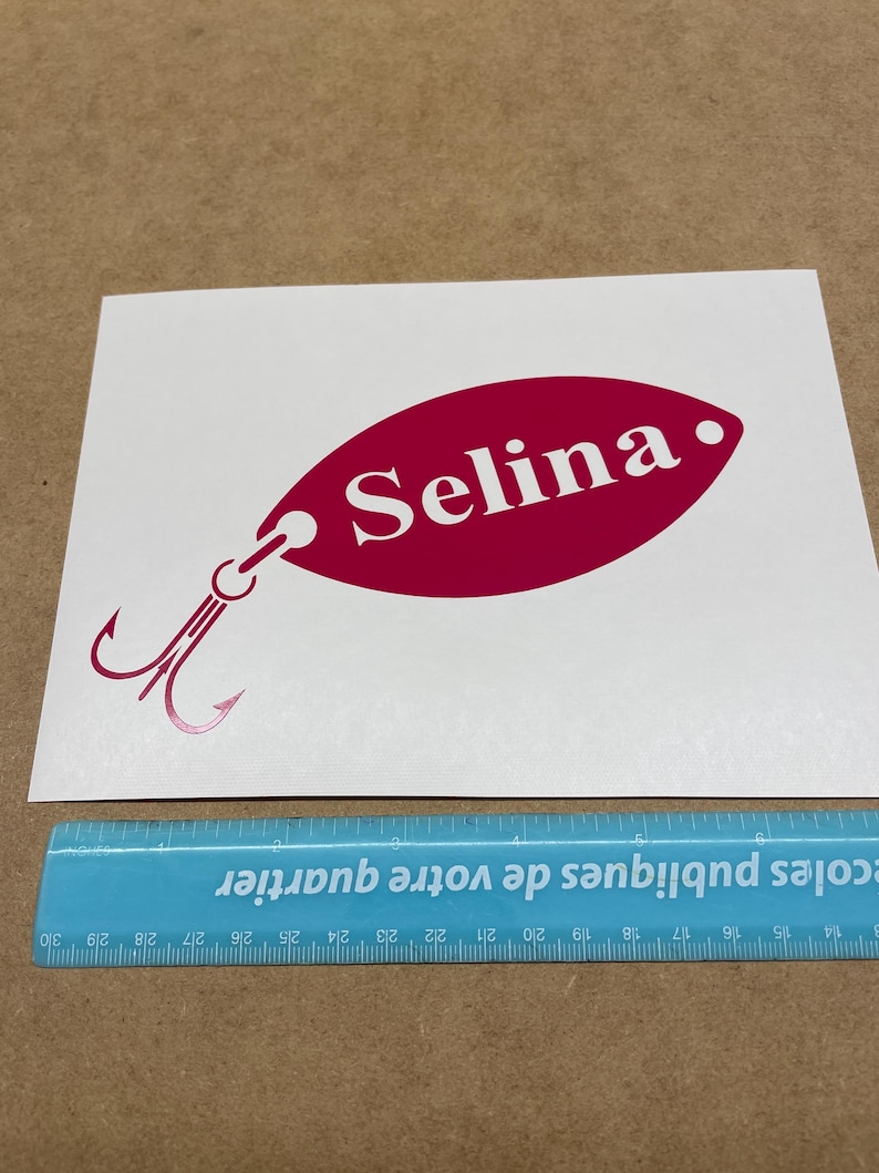 May include: A pink and white vinyl decal of a fishing lure with the name "Selina" written on it.