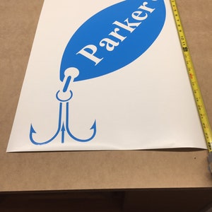May include: A white vinyl decal of a blue fishing lure with a treble hook and the name "Parker" written on it.