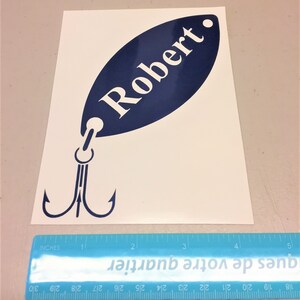 May include: A blue and white vinyl decal of a fishing lure with the name "Robert" on it. The decal is approximately 4 inches long.