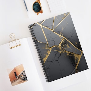 May include: A black and gold spiral notebook with a cracked marble design. The notebook has a gold spiral binding and a black cover with gold veins.