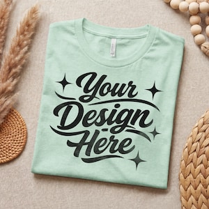 May include: A pale green t-shirt featuring the black text "Your Design Here" in a script font, with star embellishments. The shirt is neatly folded and presented on a neutral background.