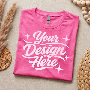 May include: A bright pink short-sleeved t-shirt featuring the white text Your Design Here in a cursive script font, accented by four-pointed star graphics. The shirt has a crew neckline and a visible brand label at the inner collar area.
