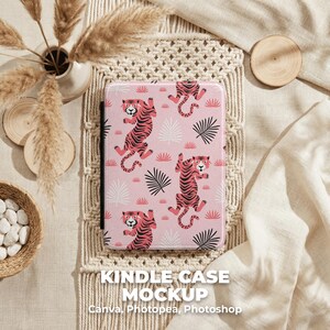 May include: Pink Kindle case with a repeating pattern of stylized tigers and black and white leaves. The case is displayed on a neutral-toned surface with the text "KINDLE CASE MOCKUP" and the names of design software.