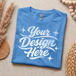 May include: A light blue t-shirt featuring the white text "Your Design Here" in a cursive script font, accented by four-pointed star graphics. The shirt has a crew neckline and a visible brand label at the inner collar, showcasing a simple design.