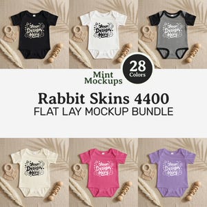 May include: A flat lay mockup bundle featuring baby onesies in various colors, including black, white, gray, cream, pink, and purple. Each onesie has the text "Your Design Here." Accompanying the onesies are wooden baby toys and dried plants. The text "Rabbit Skins 4400 FLAT LAY MOCKUP BUNDLE" is also visible.