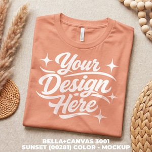 May include: A folded peach t-shirt featuring the white text "Your Design Here". The Bella+Canvas 3001 mockup is in the Sunset (00281) colour. The shirt is displayed on a neutral surface with decorative elements.