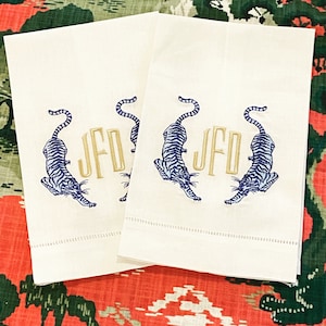 Puede incluir: Dos toallas de mano de lino blanco con tigres bordados en azul y blanco que flanquean el monograma "JFD" en hilo dorado.