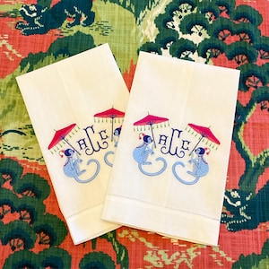 May include: Two white linen tea towels with embroidered monkeys holding red and white umbrellas. The towels have the letters "A E" embroidered in blue.