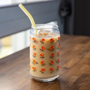 May include: A glass with a floral pattern filled with iced coffee and a yellow straw. The glass has a floral pattern with orange and green flowers.