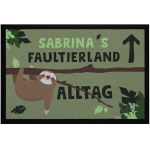 Könnte beinhalten: Eine rechteckige Fußmatte mit schwarzem Rand zeigt ein Cartoon-Faultier, das an einem Ast hängt. Der Text "SABRINA'S FAULTIERLAND ALLTAG" ist in Grün und Schwarz dargestellt. Grüne Blätter und ein Pfeil vervollständigen das Design.