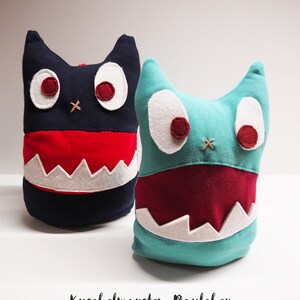 May include: Two plush monster toys with big eyes and toothy grins. One is blue with a red mouth and the other is black with a red mouth. The text "Kuschelmonster Paulechen" and "Nähnanleitung / Schnittbogen" is below the toys.