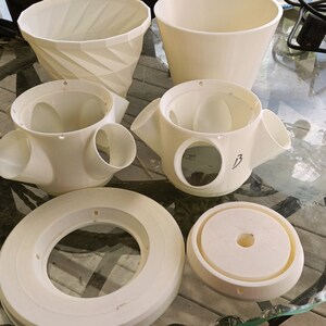 May include: A set of white plastic planter parts, including a base, a top, and a middle section with three holes. The middle section has the number "3" written on it.