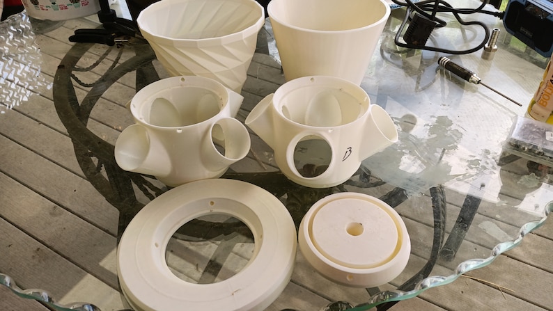 May include: A set of white plastic planter parts, including a base, a top, and a middle section with three holes. The middle section has the number "3" written on it.