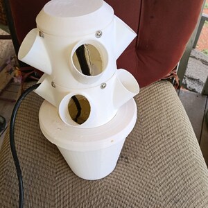 May include: White plastic vertical garden planter with multiple planting holes. The planter is connected to a black electrical cord.