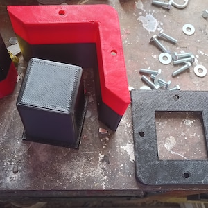 Op de afbeelding: Drie 3D-geprinte plastic hoekstukken, één zwart en twee met rode en zwarte accenten. De stukken zijn ontworpen om aan elkaar te worden bevestigd om een ​​hoekplank of een andere structuur te creëren.