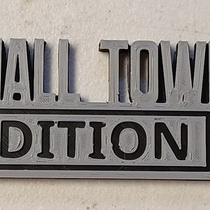 May include: A gray 3D printed sign with the text "SMALL TOWN EDITION" in black.