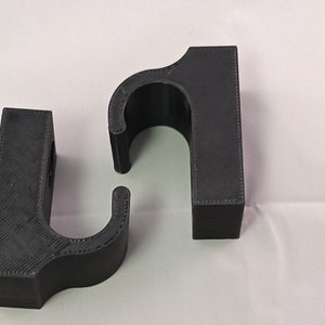 Pode incluir: Dois ganchos de parede de plástico preto com um design curvo. Os ganchos são feitos de um material texturizado e têm um visual simples e moderno.