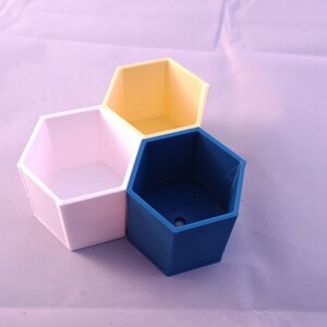 May include: Three hexagonal planters in different colors: white, yellow, and blue. The planters are arranged in a triangular shape.