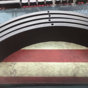 May include: Three black, curved, wooden pieces stacked on top of each other. The pieces have a smooth, polished finish and are slightly rounded on the edges. The pieces are sitting on a red, white, and blue striped surface.