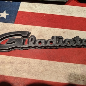 Op de afbeelding: Een zwart 3D-geprint woord "Gladiator" met een verhoogd, gestructureerd oppervlak.