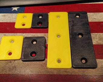 May include: Five plastic wall mount brackets, two yellow and three black, with two holes each. The brackets are arranged in a row on a red, white, and blue striped surface.