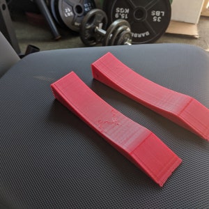 以下が含まれることがあります： 2つの赤いプラスチック製のくさび形のランプ。ランプは湾曲しており、滑らかでわずかにテクスチャ加工された表面をしています。