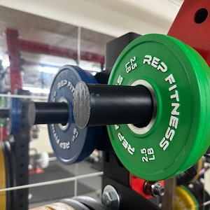 May include: A close-up of a green weight plate with the text "REP FITNESS" and "2.5 LB" printed on it. The plate is attached to a black barbell.