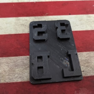 May include: A black plastic mold with the numbers 2, 3, 8, and 1 embossed on it.