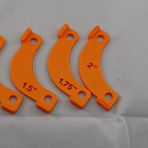 May include: Four orange plastic measuring guides with different sizes: 1.25 inches, 1.5 inches, 1.75 inches, and 2 inches.