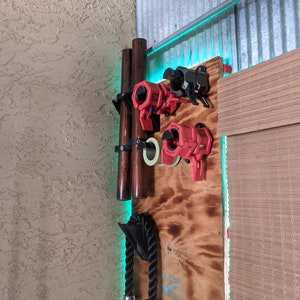 Peut inclure: Un support mural en bois avec une corde, deux chevilles en bois et quatre pinces rouges et noires. Le support est monté sur un panneau en bois avec une finition brun clair. L'arrière-plan est un mur texturé avec un éclairage d'accentuation vert clair.