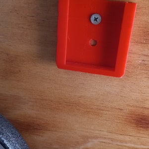 May include: A red plastic bracket with a screw hole and a silver screw in the center.