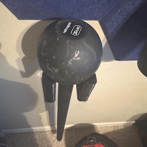 Puede incluir: Una pelota de medicina negra de 20 libras con la palabra "retrospec" impresa en ella, montada en un soporte de pared negro.