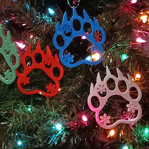 May include: Four bear paw print Christmas ornaments in different colors: green, red, blue, and white. Each ornament has a snowflake design.