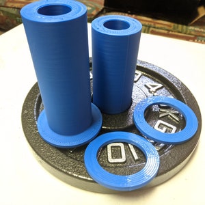 May include: Two blue plastic weight plate collars, one larger and one smaller, are on top of a black weight plate with the number 45 printed on it. The weight plate is on a white surface.