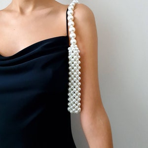 May include: A white pearl strap handbag with a black dress in the background.
