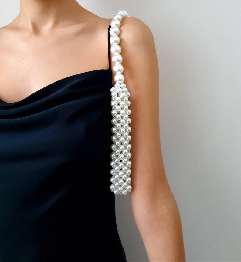 May include: A white pearl strap handbag with a black dress in the background.