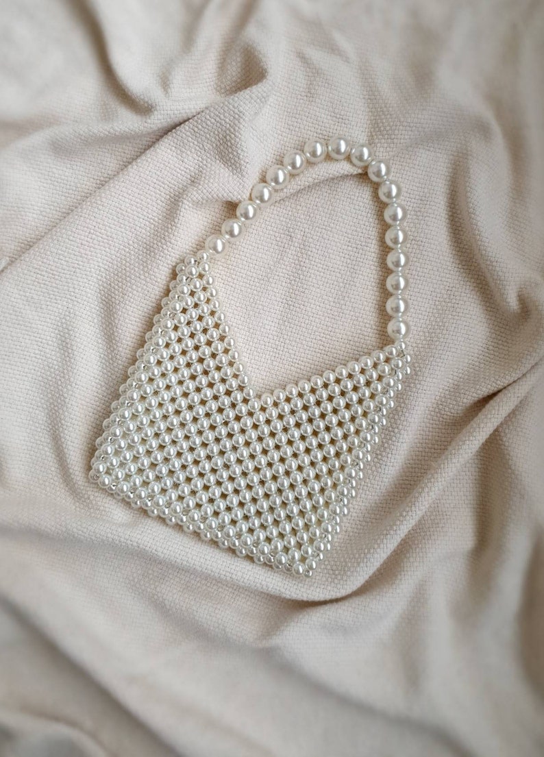 May include: A white pearl beaded bag with a triangular shape and a single pearl strap.