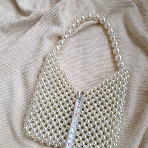 May include: A white pearl beaded handbag with a top handle. The bag is approximately 11 inches wide.