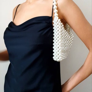 May include: A white pearl beaded handbag with a shoulder strap. The bag is small and has a rectangular shape.