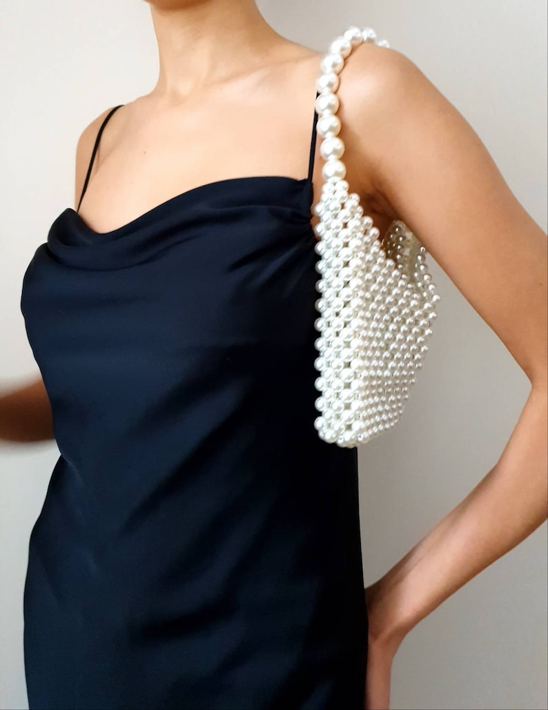 May include: A white pearl beaded handbag with a shoulder strap. The bag is small and has a rectangular shape.
